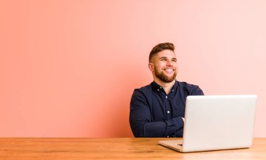 Young man working with his laptop smiling confident with crossed arms.