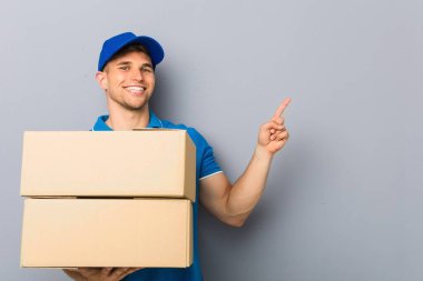 Young man delivering packages smiling cheerfully pointing with forefinger away. clipart