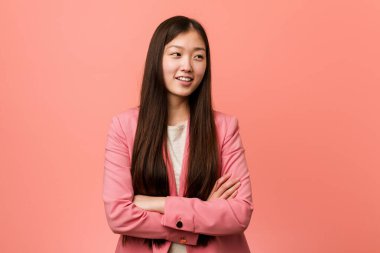 Pembe takım elbiseli genç Çinli kadın kollarını kavuşturarak gülümsüyor..