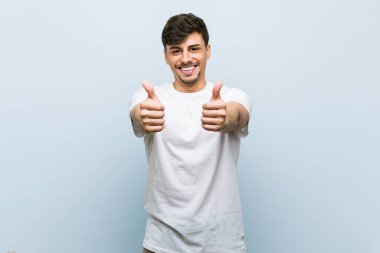 Beyaz tişörtlü beyaz beyaz bir adam. Başparmakları havada. Bir şey için tezahürat yapıyor..