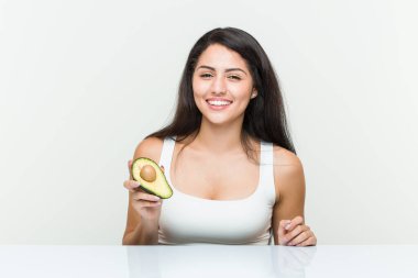 Avokado tutan genç İspanyol kadın gülümsüyor ve başparmağını kaldırıyor.