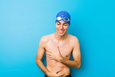 Genç yüzücü mutlu bir şekilde gülüyor ve ellerini karnının üstünde tutarak eğleniyor..