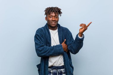 Genç Afrikalı pijama giyen siyah adam işaret parmağıyla işaret ederek gülümsüyor..