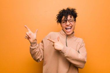 Young mixed african american woman against a brown background pointing with forefingers to a copy space, expressing excitement and desire.