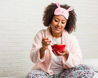 Genç afrikalı amerikalı kadın yatakta bir tahıl kase yemek