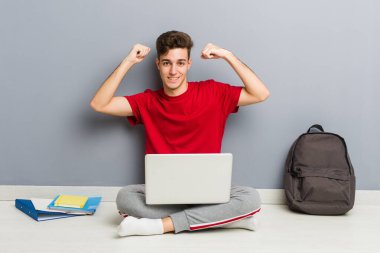 Evinin zemininde dizüstü bilgisayar tutan genç bir öğrenci.