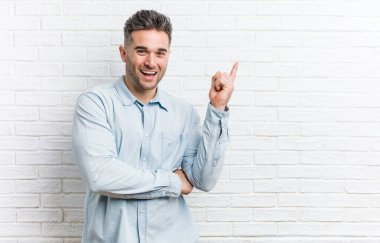 Duvara yaslanmış genç yakışıklı adam işaret parmağıyla işaret ederek gülümsüyor..