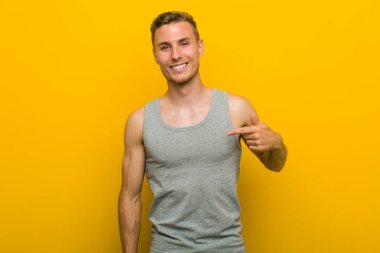 Beyaz tenli genç sporcu gömleğinin fotokopi odasını elle gösteriyor, gururlu ve kendinden emin.