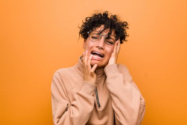 Young mixed african american woman against a brown background whining and crying disconsolately.