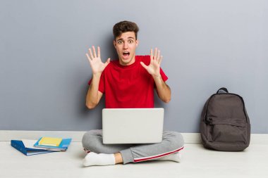 Evinin zemininde dizüstü bilgisayar tutan genç bir öğrenci.