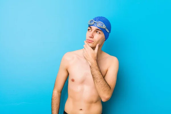 Young swimmer man looking sideways with doubtful and skeptical expression.