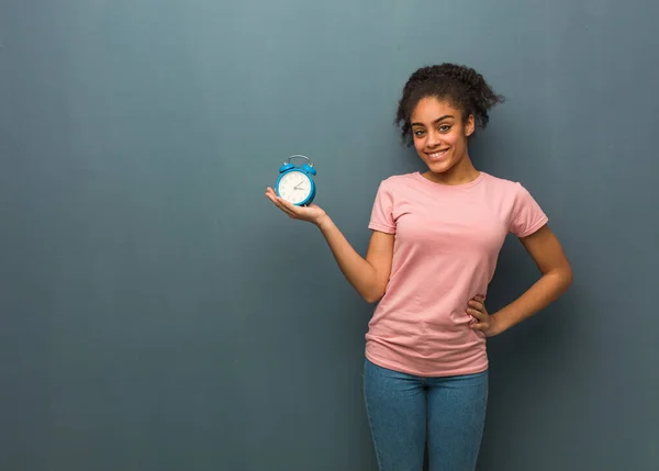 Young black woman holding something with hand. She is holding an alarm clock.