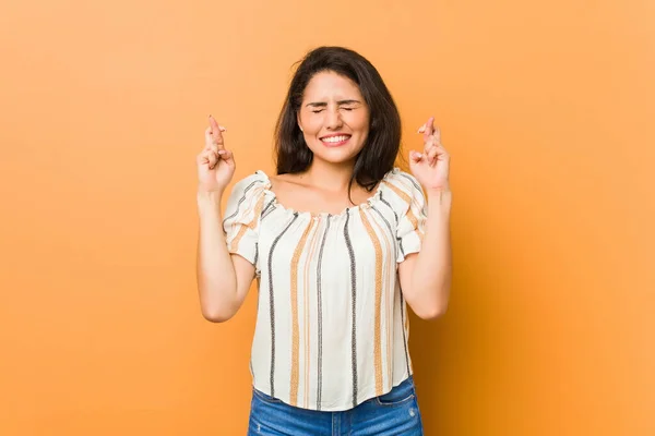 Young curvy woman crossing fingers for having luck