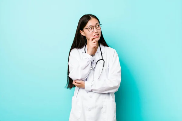 Young chinese doctor woman relaxed thinking about something looking at a copy space.
