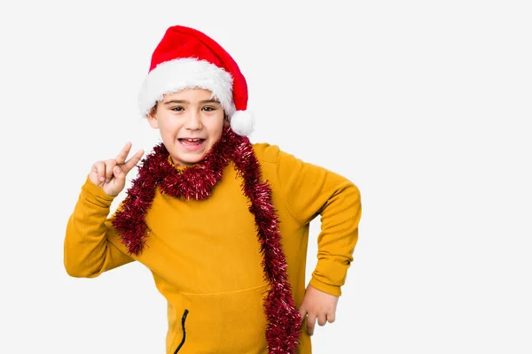 勝利の印を示す隔離されたサンタの帽子を身に着けているクリスマスの日を祝う小さな男の子と笑顔広く — ストック写真