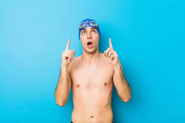 Young swimmer man pointing upside with opened mouth.