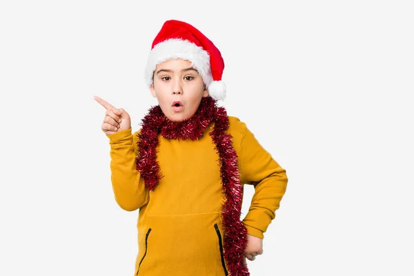 小さな男の子お祝いクリスマスの日を身に着けていますサンタの帽子隔離されたポインティング側面 — ストック写真