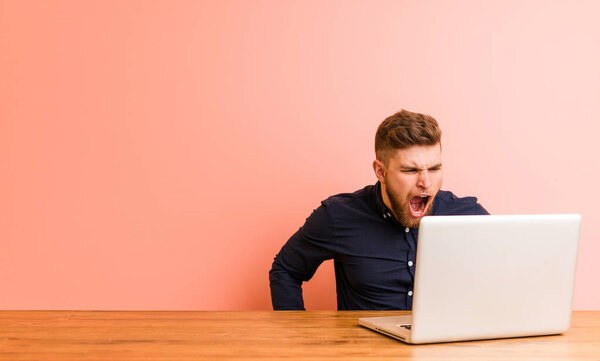 Молодой человек, работающий со своим ноутбуком, кричит очень злой и агрессивный
.