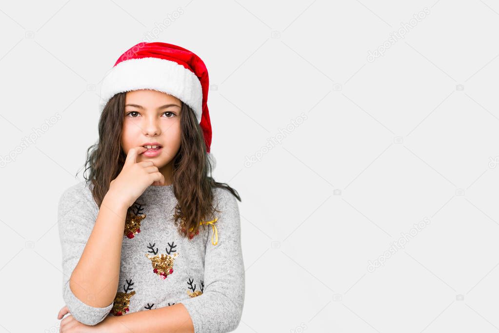 Little girl celebrating christmas day relaxed thinking about something looking at a copy space.