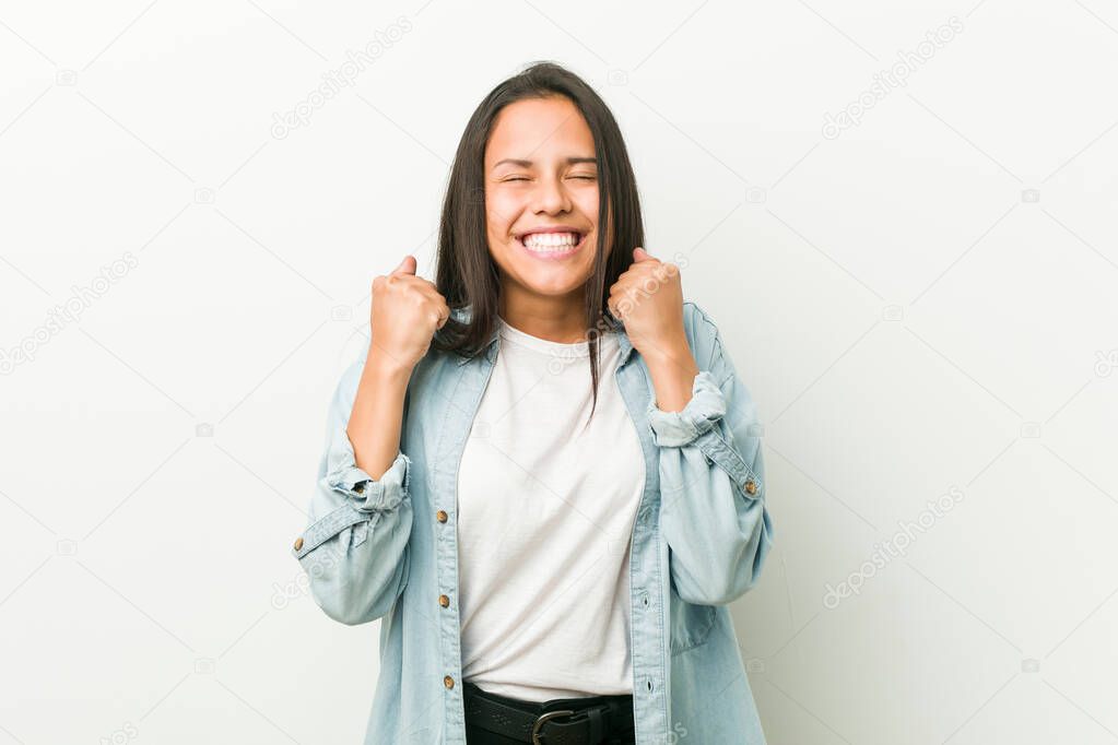 Young hispanic woman raising fist, feeling happy and successful. Victory concept.