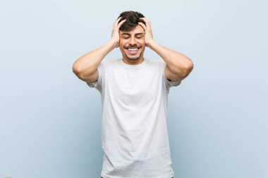 Beyaz tişört giyen genç beyaz bir adam ellerini başının üstünde tutarak neşeyle gülüyor. Mutluluk kavramı.