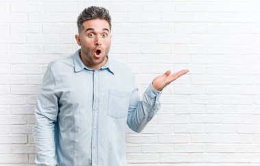 Duvara karşı duran yakışıklı genç adam, avuç içi fotokopi alanını elinde tutmaktan etkilendi..