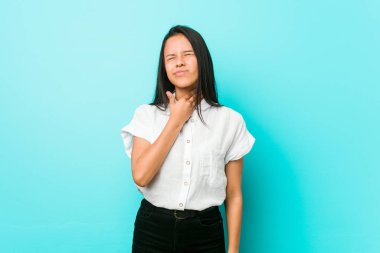 Mavi bir duvara dayanmış genç Latin asıllı havalı kadın virüs ya da enfeksiyon yüzünden boğaz ağrısı çekiyor..