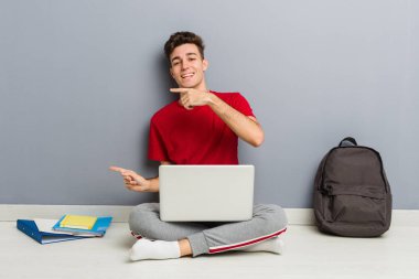 Evinin zemininde dizüstü bilgisayar tutan genç bir öğrenci.