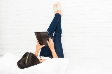 Tablet kullanarak yatakta yatan genç Arap kadın