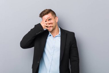 Genç yakışıklı beyaz adam kameraya parmaklarıyla göz kırpıyor, yüzünü kapatmaktan utanıyor..