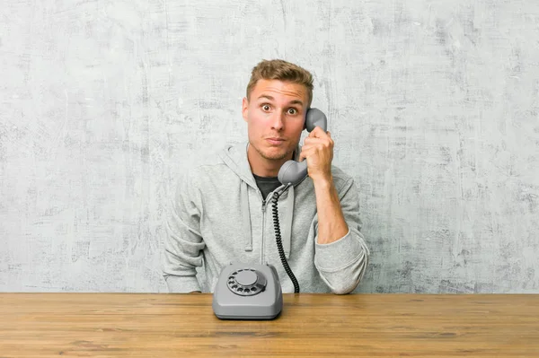 Young man talking on a vintage phone shrugs shoulders and open eyes confused.