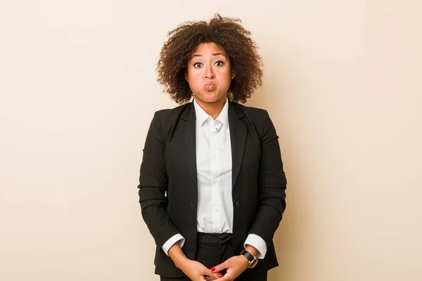 Young business african american woman blows cheeks, has tired expression. Facial expression concept.