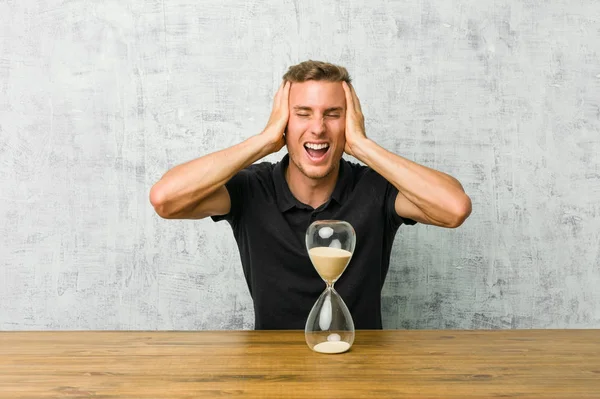 Young Man Holding Sand Timer Table Laughs Joyfully Keeping Hands — Stock Photo, Image