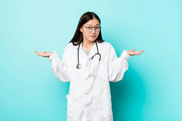 Young chinese doctor woman doubting and shrugging shoulders in questioning gesture.
