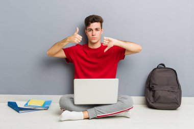 Evinin zemininde dizüstü bilgisayar tutan genç bir öğrenci.