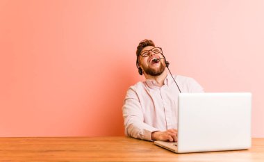 Çağrı merkezinde çalışan genç bir adam gevşemiş ve mutlu bir şekilde gülüyor, boynunda dişlerini gösteriyor..