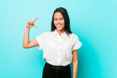 Mavi duvara yaslanmış, gülümseyen ve kendine güveni olan küçük bir şey tutan İspanyol asıllı havalı bir kadın..