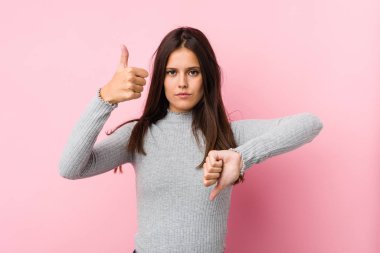 Genç, sevimli bir kadın baş parmağını kaldırıyor ve baş parmak aşağı, zor seçim konsepti.