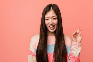 Genç, havalı Çinli kadın göz kırpıyor ve elleriyle iyi bir jest yapıyor..