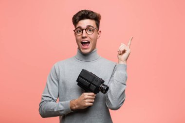 Genç entellektüel bir adam, elinde bir film kamerasıyla mutlu bir şekilde işaret parmağıyla işaret ediyor..