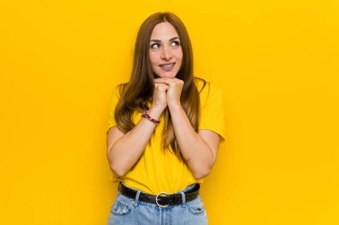 Kızıl saçlı genç kadın ellerini çenesinin altında tutuyor ve mutlu bir şekilde yan tarafa bakıyor..