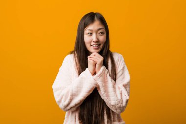 Pijamalı genç Çinli kadın ellerini çenesinin altında tutuyor ve mutlu bir şekilde yan tarafa bakıyor..