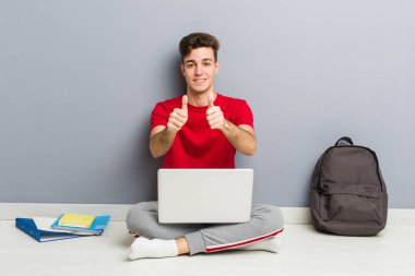 Evinin zemininde dizüstü bilgisayar tutan genç bir öğrenci.