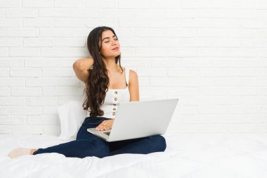 Yatakta dizüstü bilgisayarıyla çalışan genç bir Arap kadın sabit yaşam tarzından dolayı boyun ağrısı çekiyor..