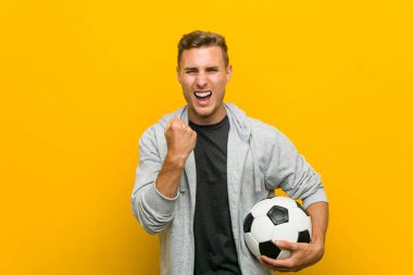 Kafkasyalı genç bir adam futbol topu tutuyor tasasız ve heyecanlı bir şekilde tezahürat yapıyor. Zafer konsepti.