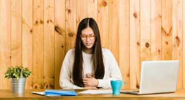 Genç Çinli kadın masasında hasta yatıyor, karın ağrısı çekiyor, acı verici hastalık konsepti var..