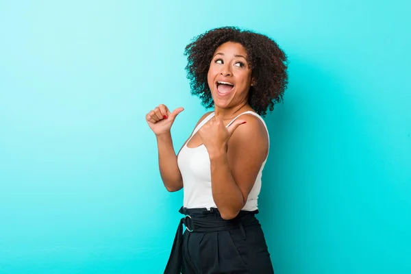 Young african american woman points with thumb finger away, laughing and carefree.