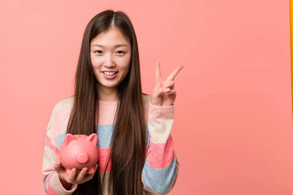 Mladá Asijská Žena Drží Prasátko Banka Ukazující Číslo Dvě Prsty — Stock fotografie