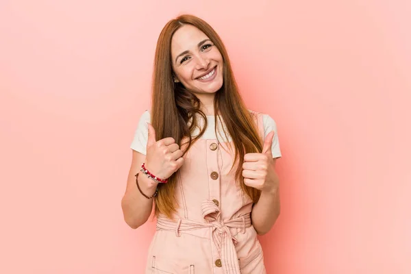 Young ginger woman with freckles raising both thumbs up, smiling and confident.