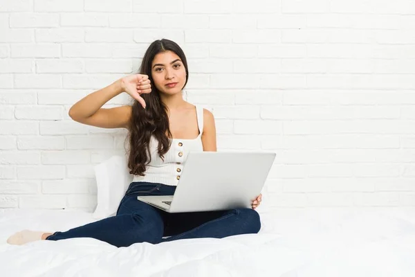 ベッドの上でノートパソコンを操作している若いアラブ人女性は嫌なジェスチャー 親指を下に示しています 意見の相違 — ストック写真